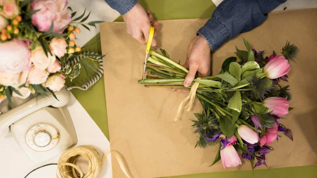 A florist cutting flowers' stems and wrapping them in a beautiful bouquet.